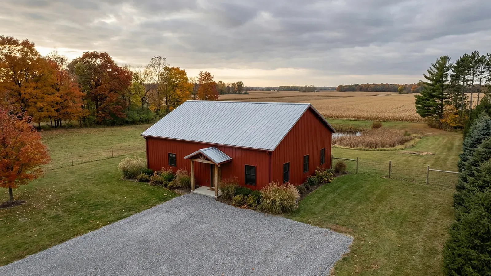 A compact 30x40 barndominium sized like a starter home or cabin, with a covered entry porch and autumn maples at the edge of the yard.