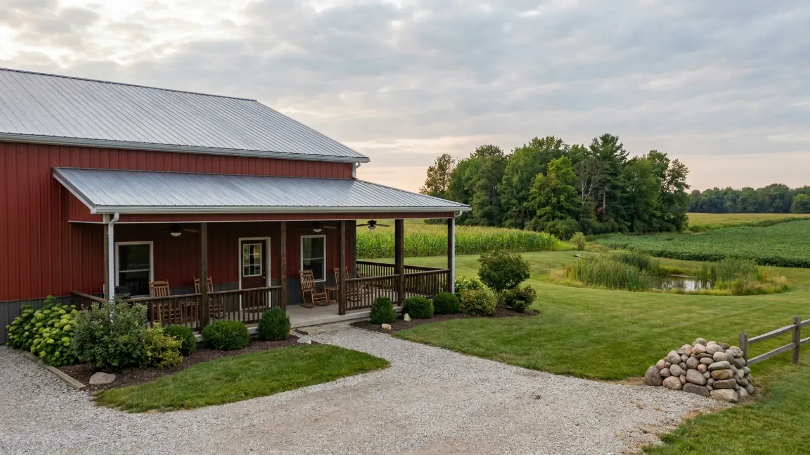 A barndominium exterior showing a deep wrap-around covered porch with posts and railing along two sides of the building.
