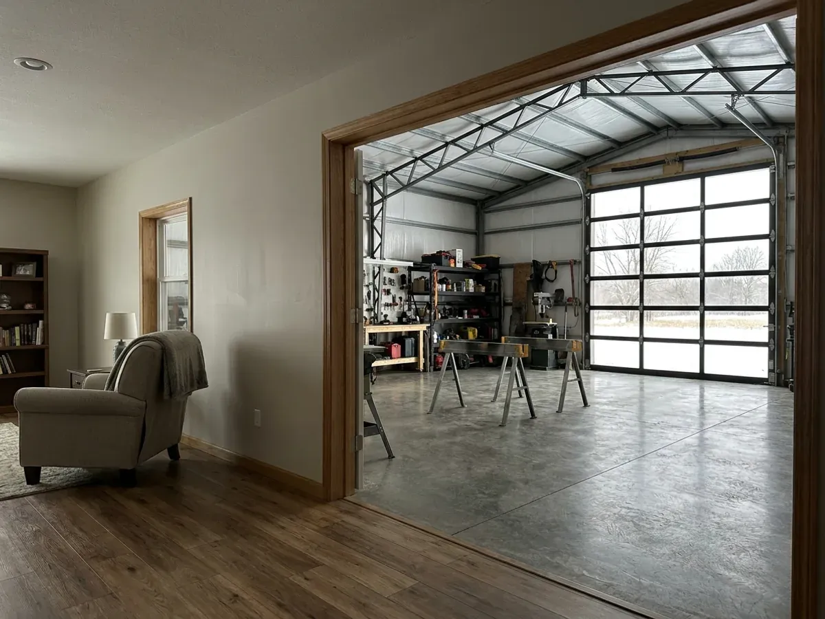 The interior of a shouse where a finished living area with warm flooring meets a shop bay with sealed concrete and a tall roll-up door.